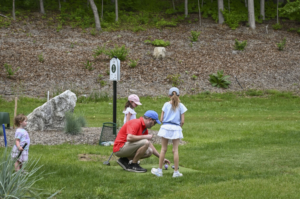 Father playing park golf with his daughters at 1Club in Vernon Valley, New Jersey, on a warm summer day.