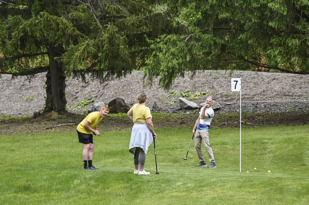 Three people having fun while playing park golf at 1Club in Vernon, NJ, smiling and enjoying the game on the scenic course surrounded by lush greenery.