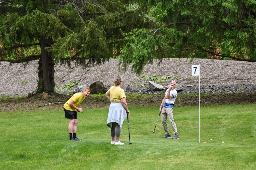 Three people having fun while playing park golf at 1Club in Vernon, NJ, smiling and enjoying the game on the scenic course surrounded by lush greenery.